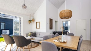 Un salon moderne avec une table à manger en bois, des canapés gris et une grande fenêtre donnant sur l’extérieur.