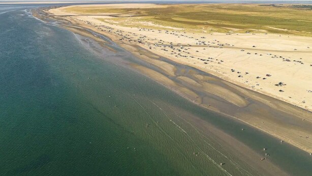 Vue aérienne d’une zone côtière avec une plage de sable et une vaste étendue d’eau.