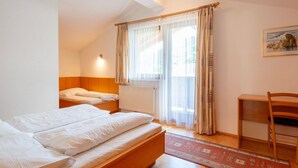 A hotel room with two beds, a wooden headboard, a radiator, a window with sheer curtains, a wooden chair, and a patterned rug. - Mountain Apartment With Balcony for Families (Uderns)