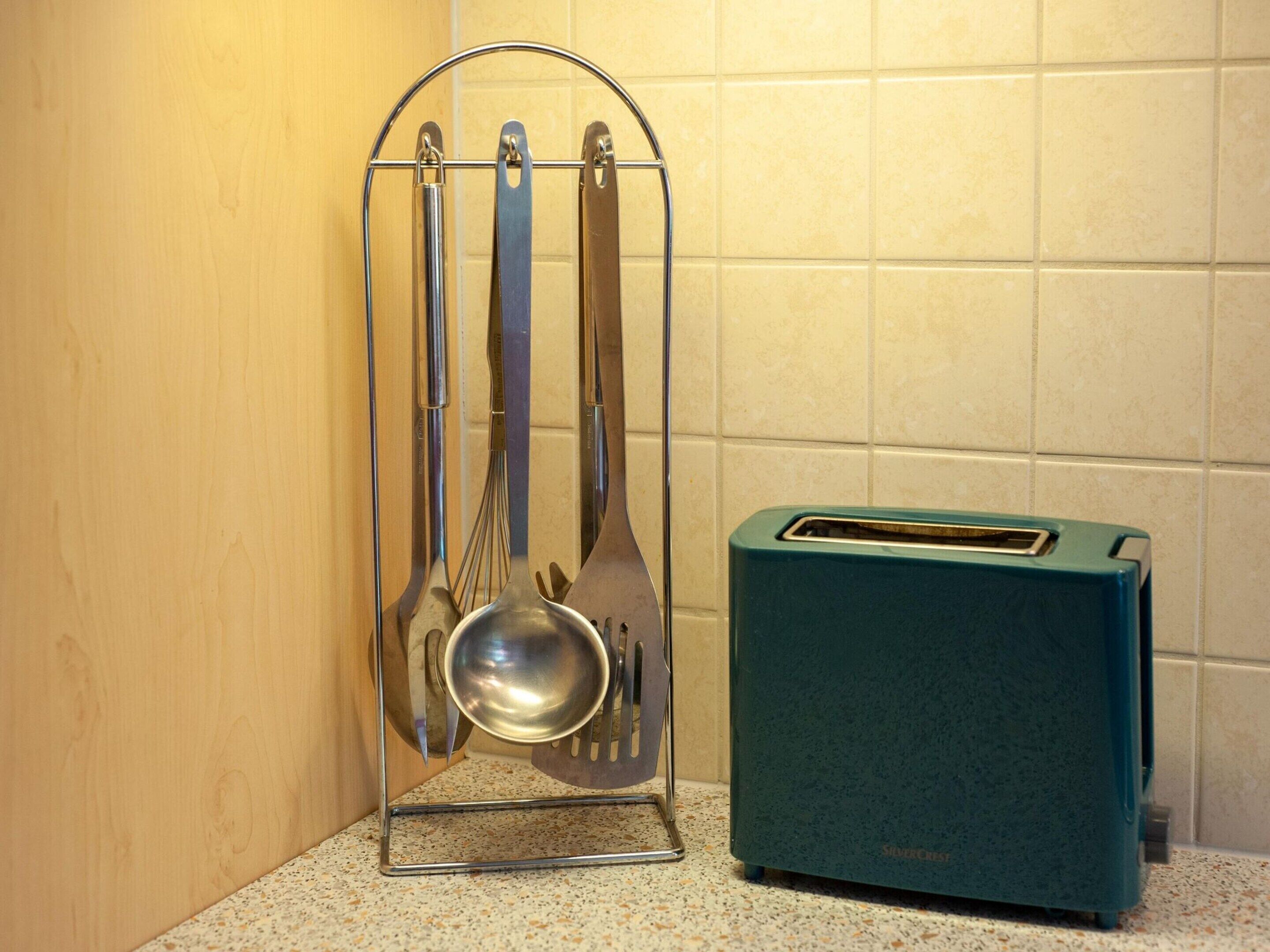 Eine Küche mit einem Utensilienhalter, der einen Schaumlöffel, einen Pfannenwender und einen Schneebesen enthält, sowie einem türkisfarbenen Toaster.