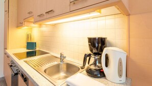 A kitchen with a stainless steel sink, a coffee maker, and a white electric kettle. - Mountain Apartment With Balcony for Families (Uderns)