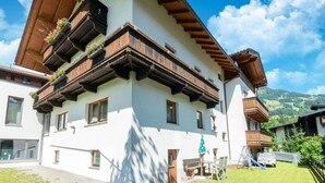 A traditional Alpine-style building with wooden balconies, a patio area, and a view of the surrounding landscape. - Mountain Apartment With Balcony for Families (Uderns)