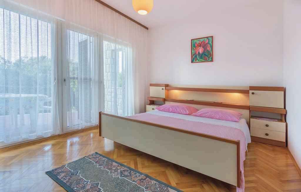 Un dormitorio con cama, mesitas de noche, un ventanal con cortinas y un cuadro en la pared.
