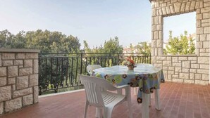 A balcony with a stone wall, a metal railing, a round table with a floral tablecloth, and two white plastic chairs. - Holiday apartment near the beach (Pješćana Uvala)