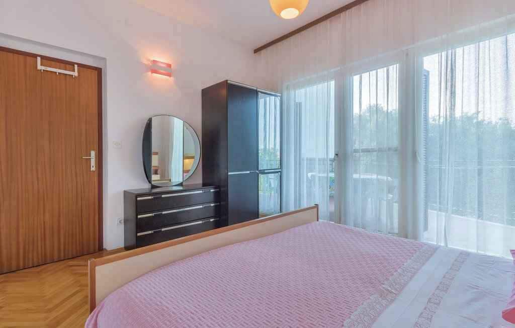 Une chambre à coucher avec un lit, une armoire, un miroir et une fenêtre avec des rideaux.