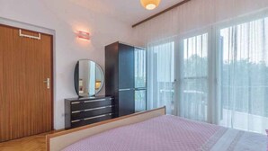 A bedroom with a bed, a wardrobe, a mirror, and a window with curtains. - Holiday apartment near the beach (Pješćana Uvala)