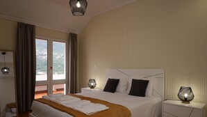 A neatly made bed with a white headboard, a bedside lamp, and a view of the outdoors through a large window.