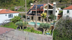 A two-story house with a swimming pool, solar panels, and a well-maintained garden.