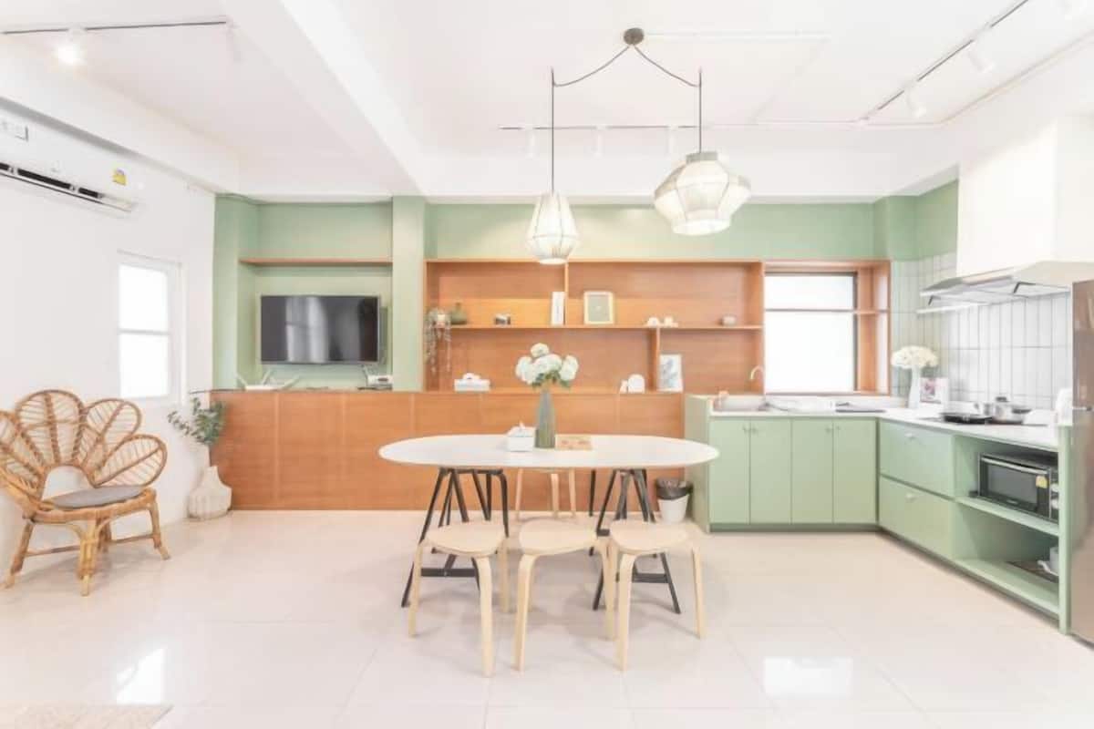Une cuisine moderne avec une table à manger ronde, des meubles de couleur verte et des luminaires suspendus.