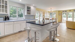 Una cocina moderna con armarios blancos, una isla grande con taburetes y vistas al exterior a través de amplias ventanas.