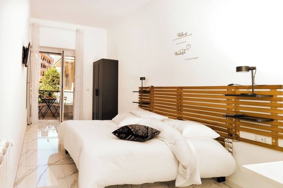 Un dormitorio con cama, cabecera de madera, estante en la pared y puerta que da a un balcón.