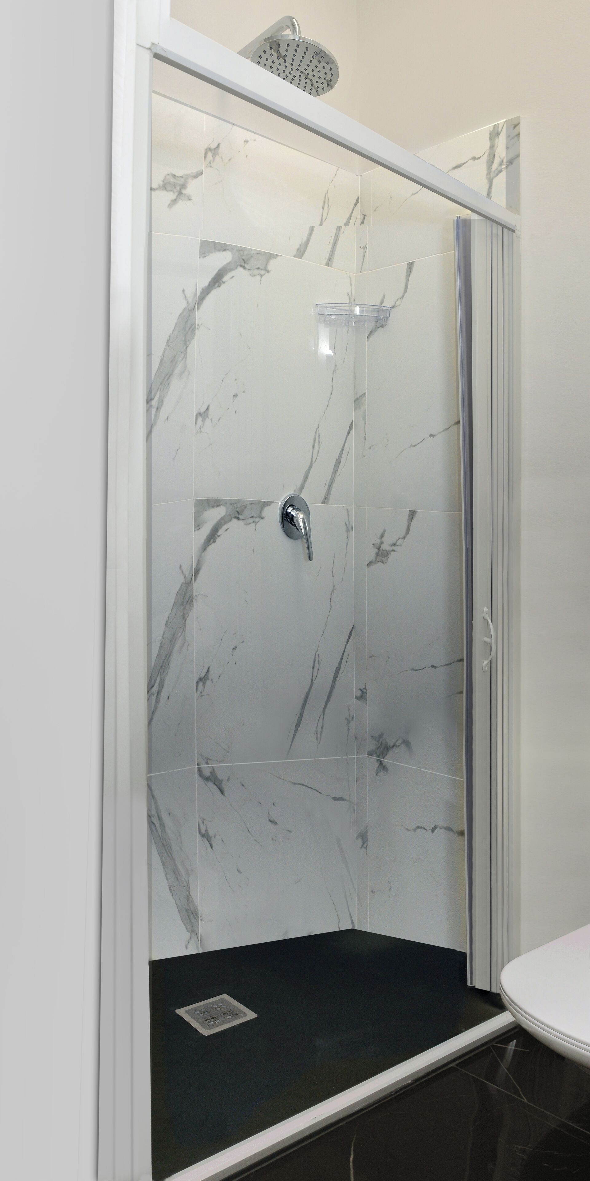 A glass-enclosed shower with a marble wall and a black floor.