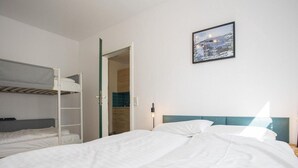 Ett hotellrum med våningssängar, en enkelsäng, ett nattduksbord med en lampa och en inramad tavla på väggen.
