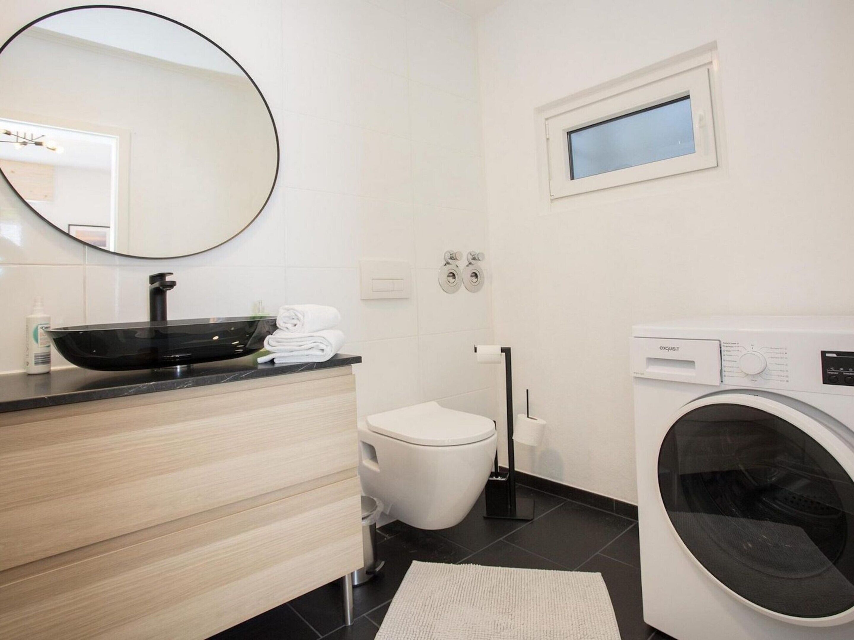 Une salle de bain moderne avec un lavabo noir, des toilettes blanches et un lave-linge à chargement frontal.