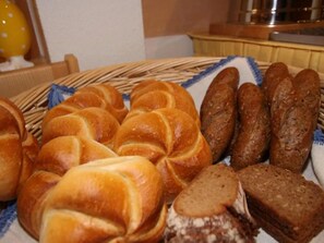 Ein Korb mit verschiedenen Brotsorten und Gebäck, darunter Croissants und Baguettes, auf einem Tisch.