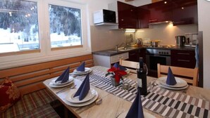 A modern kitchen with wooden beams, a dining area with a checkered tablecloth, and a view of snowy trees outside. - Klasse Apartment mit Balkon St. Anton am Arlberg (Sankt Anton am Arlberg)