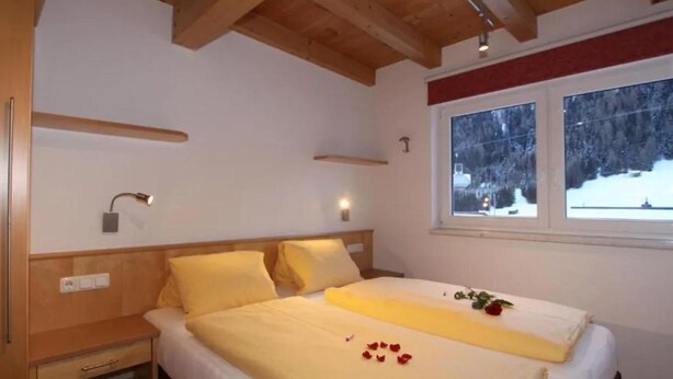 A bedroom with a wooden ceiling, a bed with yellow bedding, a bedside table, and a window with a snowy view. - Klasse Apartment mit Balkon St. Anton am Arlberg (Sankt Anton am Arlberg)