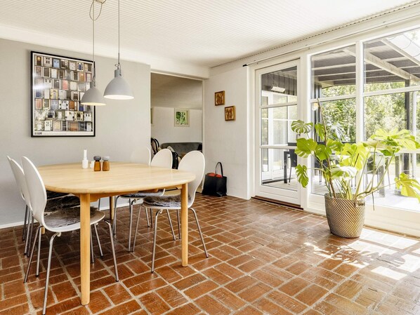 A dining area with a wooden table and chairs, a hanging light fixture, and a large window with a view of greenery.