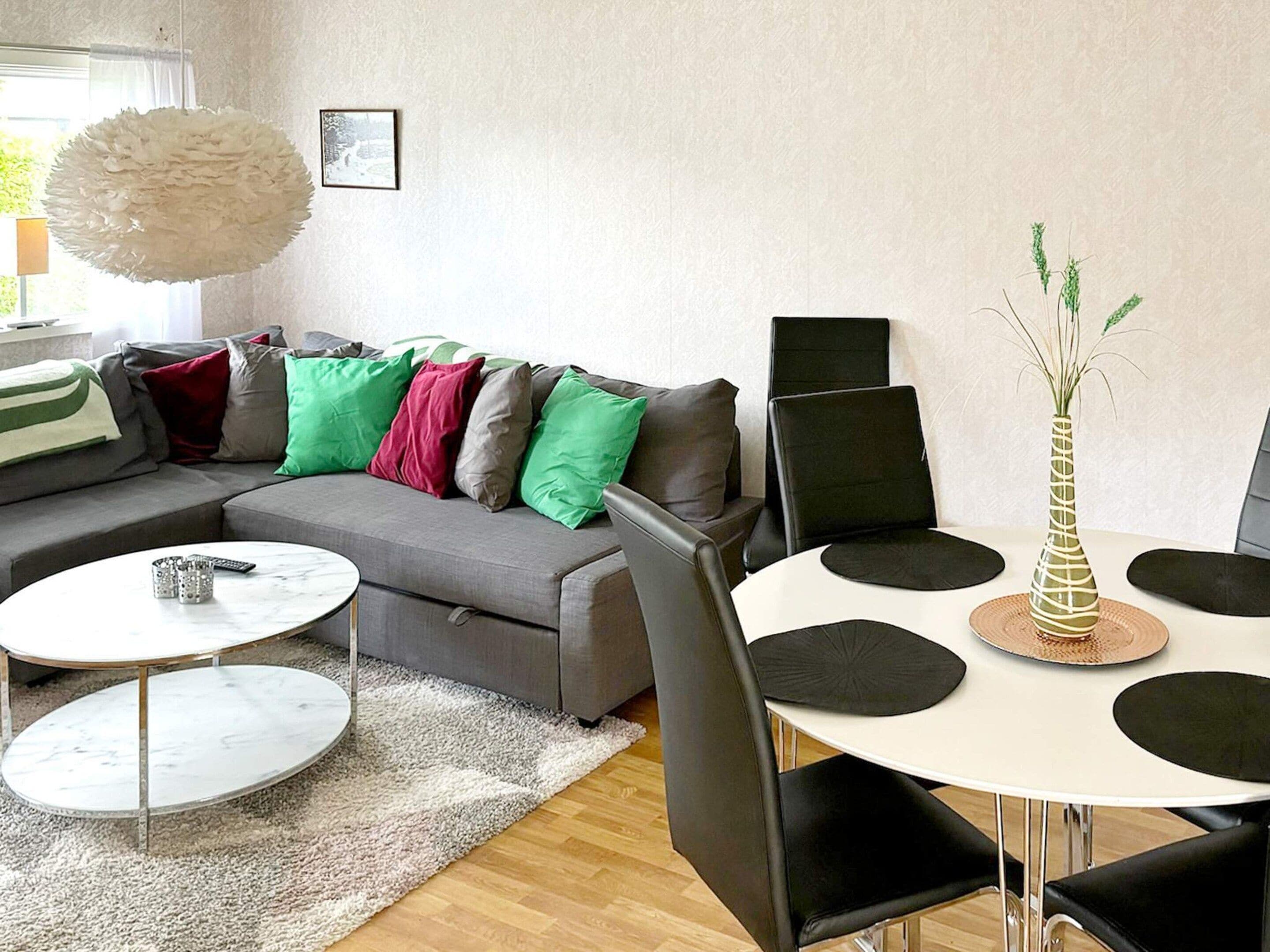 A modern living room with a grey sectional sofa, a round coffee table, a white dining table with black chairs, and a decorative vase with green plants.