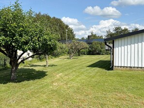 A well-maintained grassy yard with a large tree, a white building, and a clear blue sky. - 6 Person Holiday Home in Mellbystrand (Mellbystrand)
