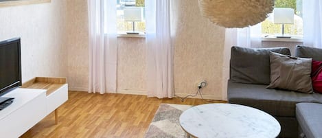 Een moderne woonkamer met een flatscreen televisie, een grijze bank, een marmeren salontafel en een grote, zachte lamp.