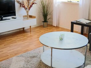 A living room with a flat-screen TV, a white sofa, a round table with two glasses, a potted plant, and a small table with a book. - 6 Person Holiday Home in Mellbystrand (Mellbystrand)