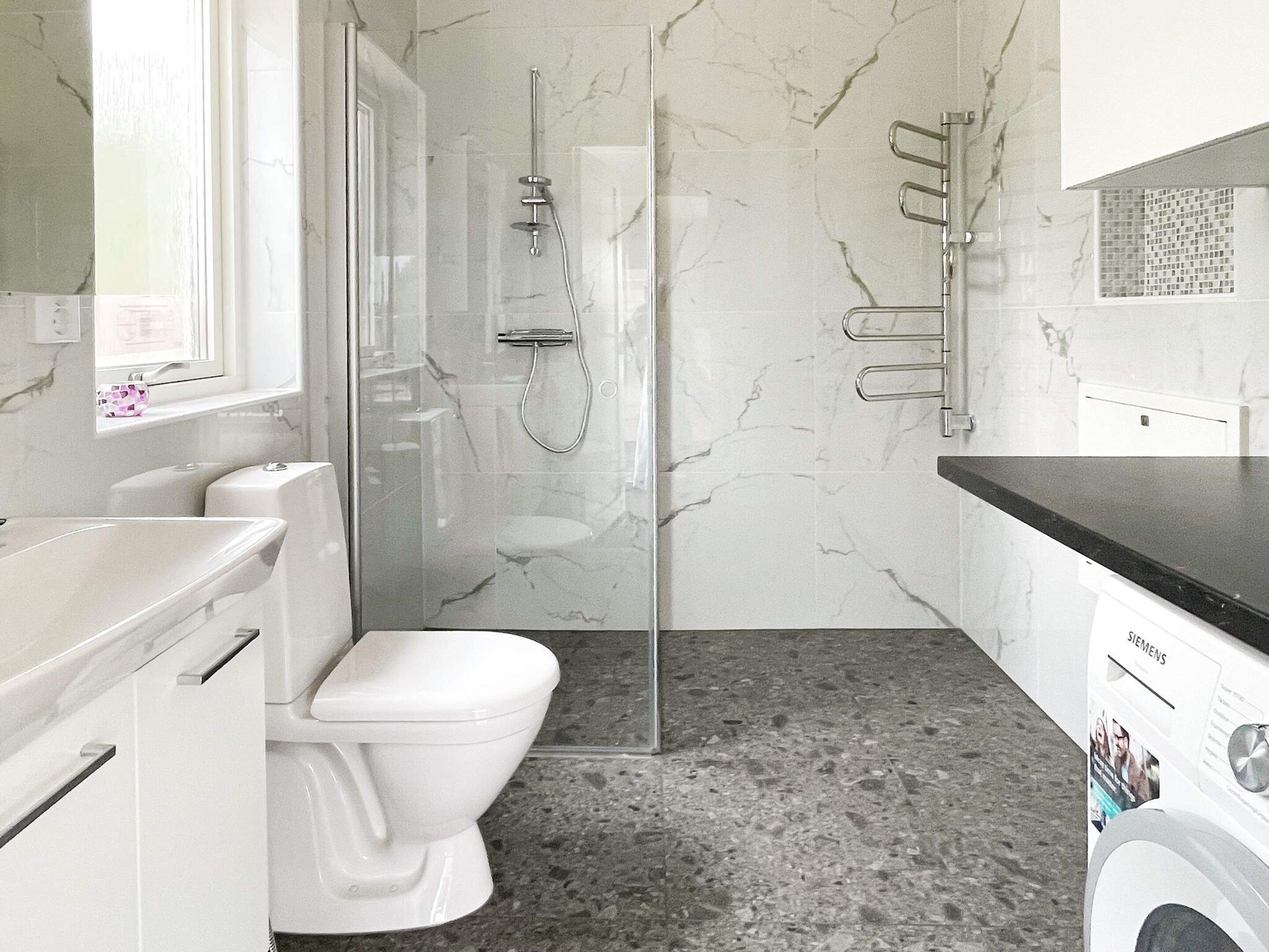 Un baño moderno con ducha envuelta en vidrio, inodoro blanco y lavadora.