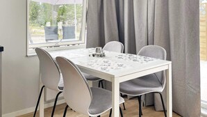 A dining area with a white table, grey chairs, a window with curtains, and an outdoor view. - 4 Star Holiday Home in Klintehamn (Klintehamn)