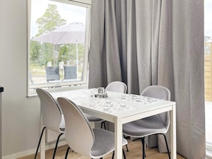 A dining area with a white table, grey chairs, a window with curtains, and an outdoor view. - 4 Star Holiday Home in Klintehamn (Klintehamn)