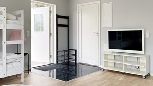 A room with a bunk bed, a TV on a white stand, a door, and a black shelf unit. - 4 Star Holiday Home in Klintehamn (Klintehamn)