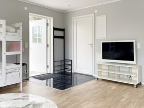 A room with a bunk bed, a TV on a white stand, a door, and a black shelf unit. - 4 Star Holiday Home in Klintehamn (Klintehamn)