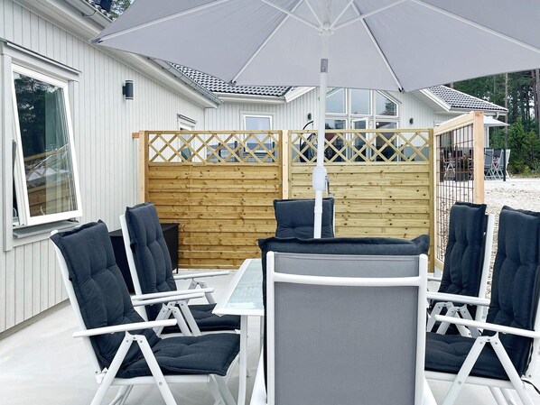 An outdoor seating area with white metal chairs and a table, a wooden fence, and a house with a tiled roof in the background. - 4 Star Holiday Home in Klintehamn (Klintehamn)