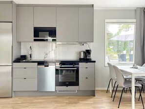 A modern kitchen with integrated appliances, a dining area with a table and chairs, and a window with a view of greenery. - 4 Star Holiday Home in Klintehamn (Klintehamn)