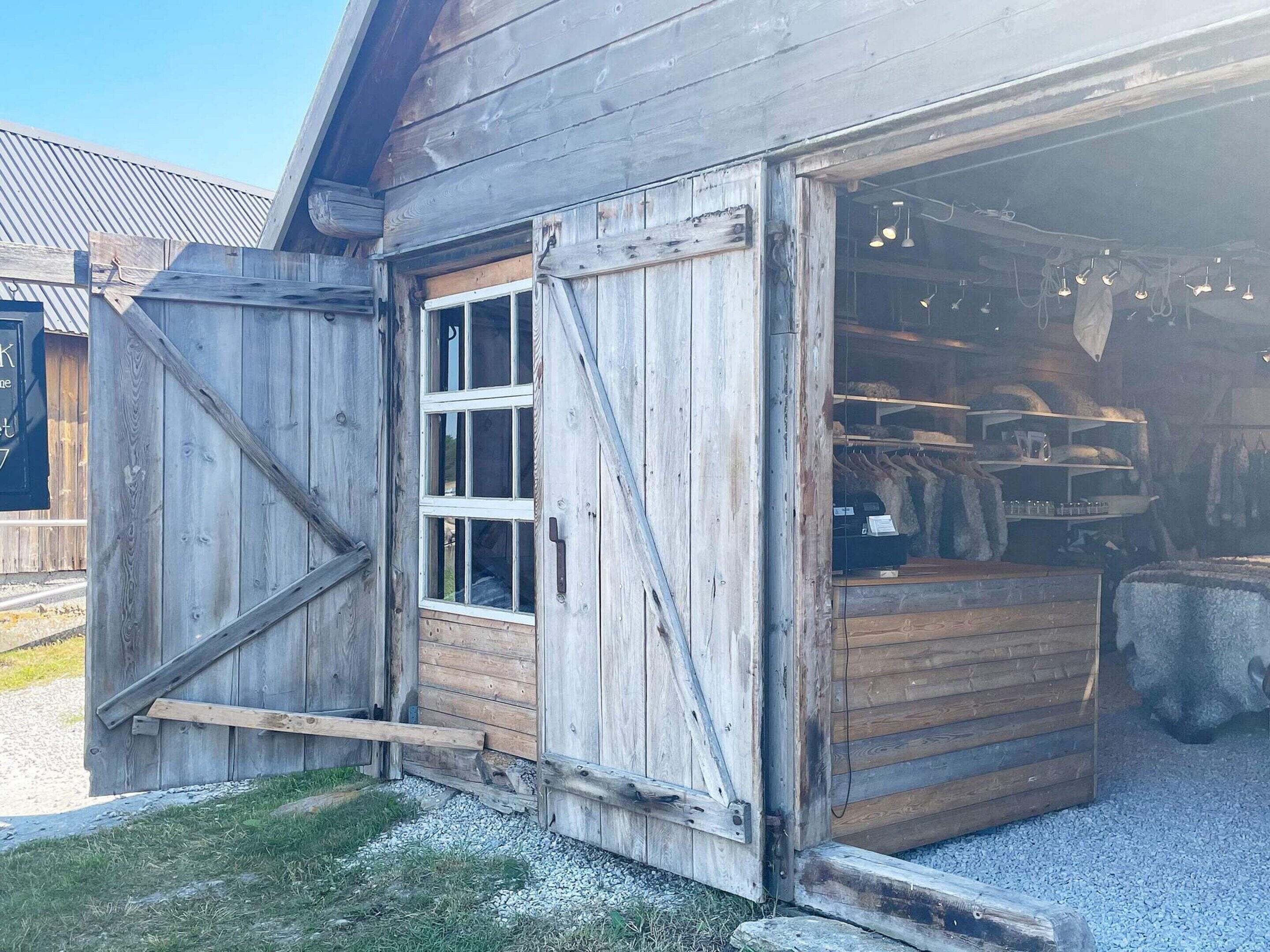 A rustic wooden building with a large open garage door, a window, and a gravel driveway.