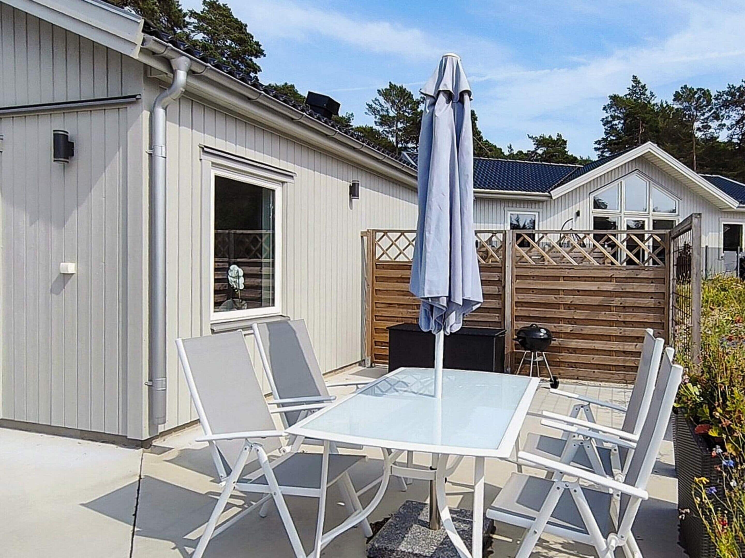 Une terrasse avec une table en verre et quatre chaises, un barbecue et une clôture en bois.