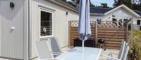 A patio with a glass table and four chairs, a barbecue grill, and a wooden fence.