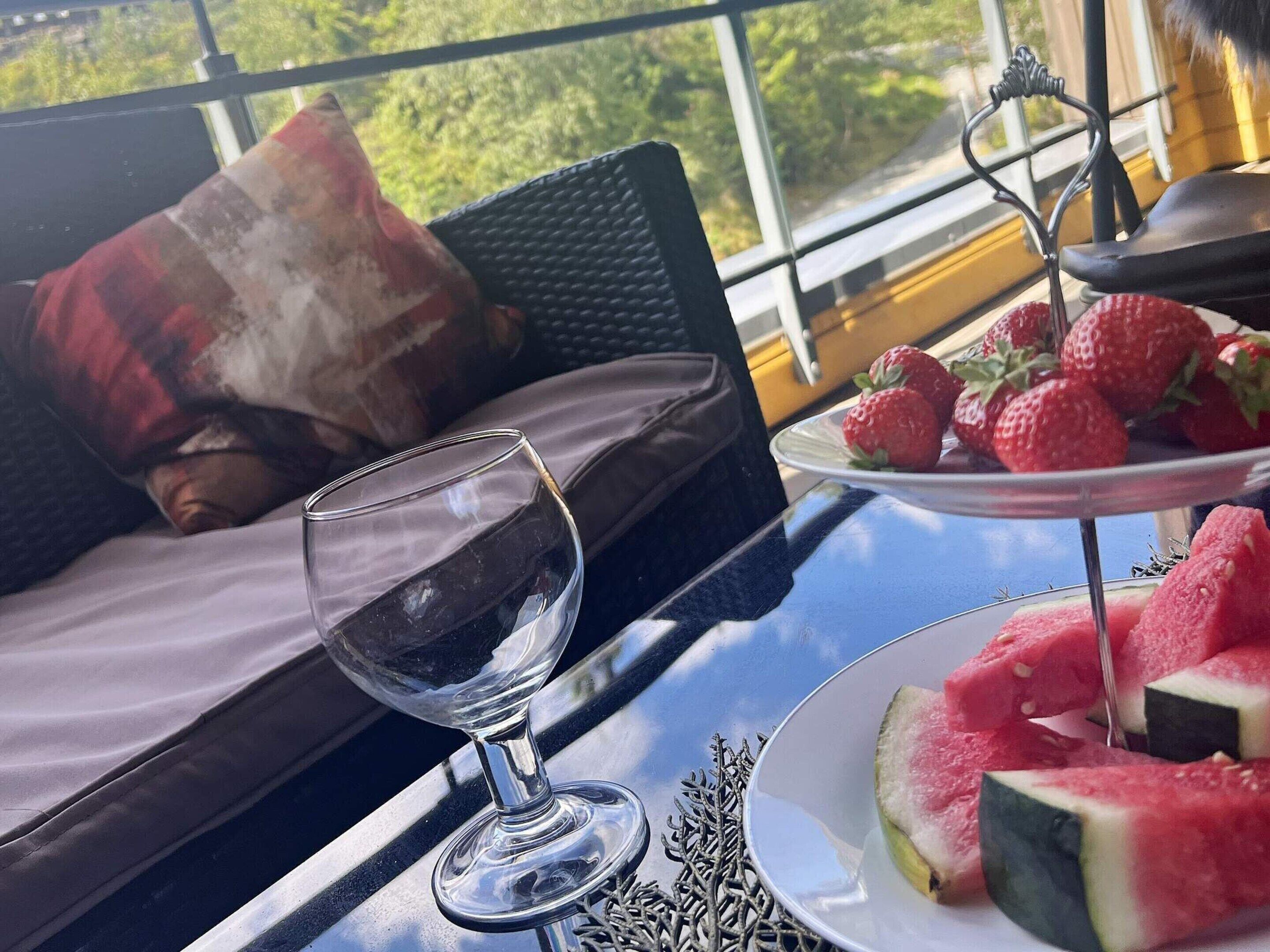A glass of red wine on a table with a plate of strawberries and watermelon slices.
