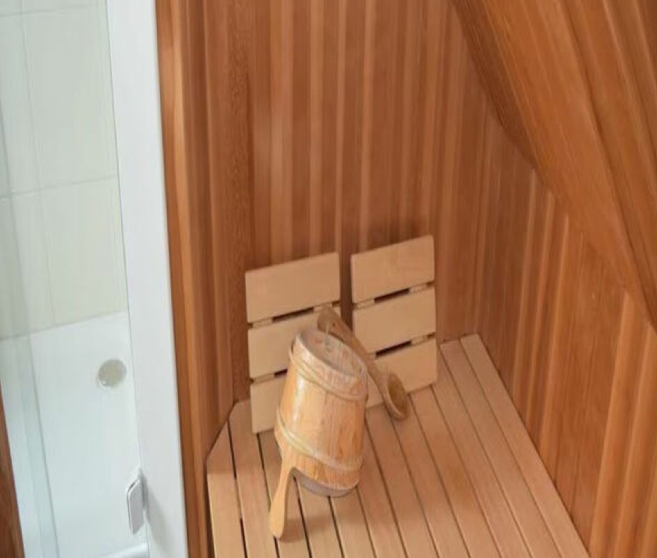 Una sauna de madera con un banco y un balde de madera.
