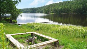 Vista de un lago con muelle de madera y estructura metálica para parrilla.