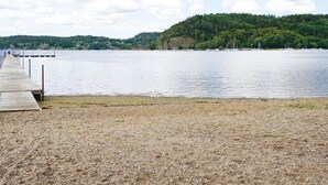 Un muelle de madera se extiende sobre un lago tranquilo con una colina boscosa al fondo.