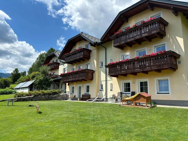A multi-story hotel with balconies adorned with flowers, a well-maintained lawn, and a clear sky.
