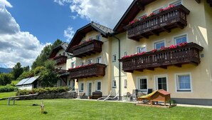 A multi-story hotel with balconies adorned with flowers, a well-maintained lawn, and a small wooden structure. - Apartment in Lungau Near Ski Lift (Sankt Michael im Lungau)