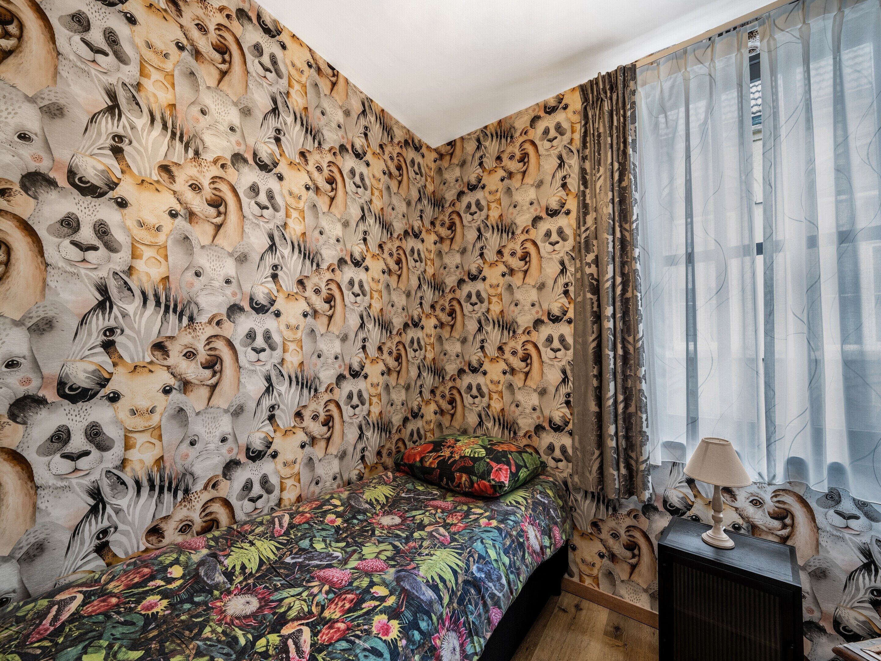 A bedroom with a bed, a nightstand, and a wall covered in animal prints.