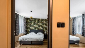 Une chambre à coucher avec un lit, un plancher en bois, un miroir et un papier peint à motifs tropicaux.