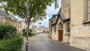 Une rue pavée bordée de bâtiments historiques, dont une église dotée d’une porte en bois et d’un clocher haut et étroit.