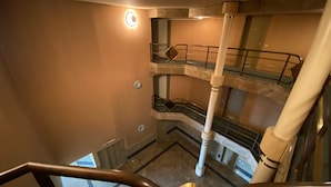 Un interior de varios niveles con una escalera, barandillas metálicas y una lámpara circular.
