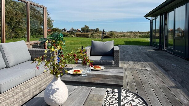 Eine Terrasse im Freien mit einer Couch, einem Esstisch mit Tellern und einer Vase mit Blumen.