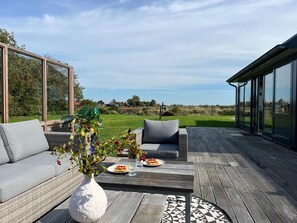 An outdoor deck with a sofa, a dining table with plates, and a vase with flowers. - Holiday Home in Texel Near De Hors Reserve (Den Hoorn)