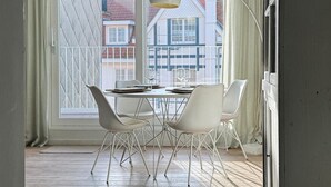 A dining area with a table and chairs, a floor lamp, and a view of buildings through large windows. - Bright Flat With Bunk Beds (De Haan)