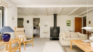 A cozy living room with a sofa, a wooden coffee table, a chair, and a fireplace. - 6 Person Holiday Home in Gilleleje (Gilleleje)